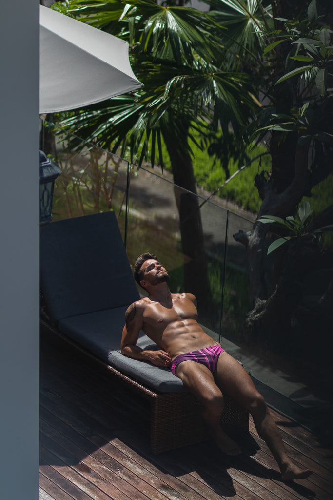 Capture attention with Smithers Swimwear's 'Doppler' men's swimsuit featuring vertical stripes in varying shades of pink and maroon. Fit young model poses confidently beside a sun-drenched backyard pool.